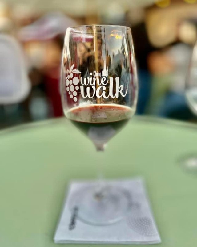 A glass of red wine with the Chino Hills Wine Walk logo etched on it, on a green table.