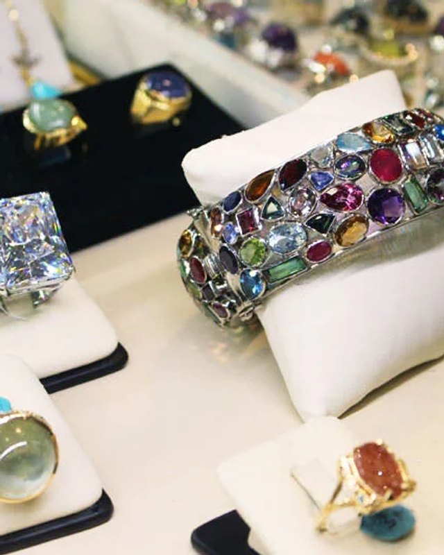 Rings and a jeweled bracelet displayed on white and black pads at a jewelry show.