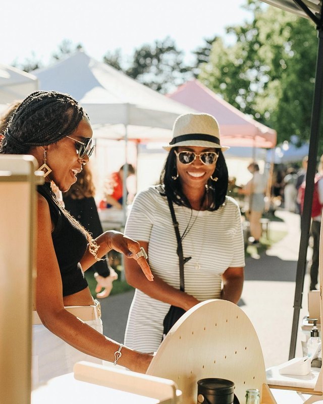 Shoppers chatting with a vendor at a market booth under white tents in Kirkland.