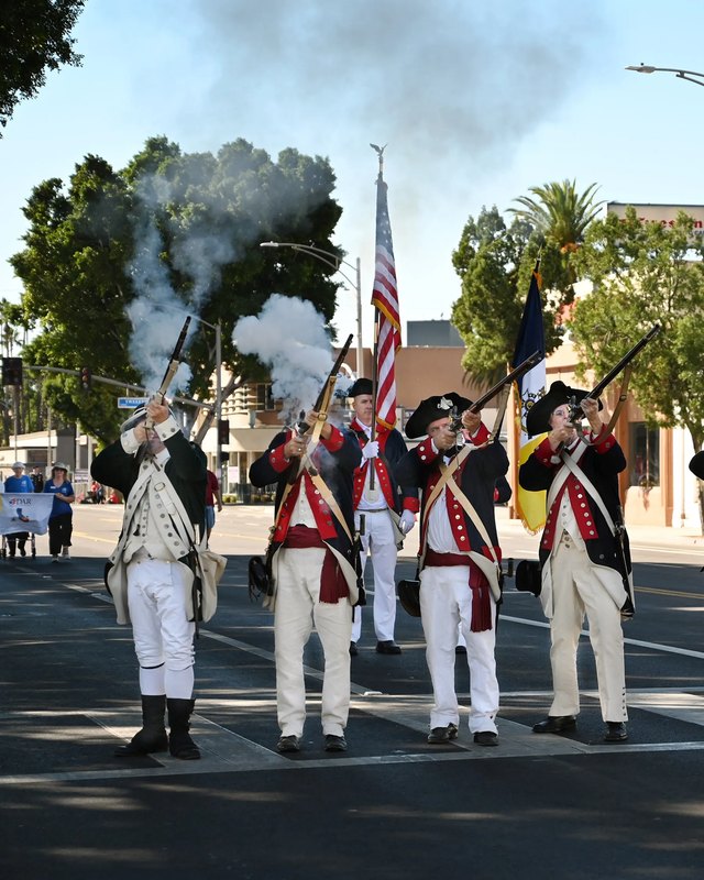 Costumed musket reenactors firing a volley during the A Salute to Veterans parade through downtown Riverside.