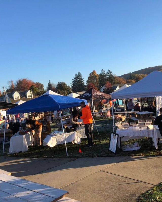 Tents and shoppers at outdoor flea market stalls on a sunny autumn day in Newington
