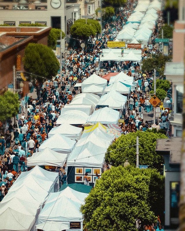 Aerial view of crowds walking between rows of white festival tents on a Union Street-style hill street.