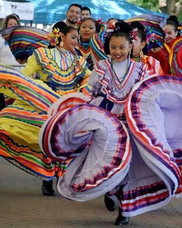Folklórico dancers in colorful full skirts performing at the Cinco de Mayo festival crowd.