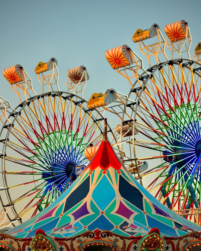 Tall Ferris wheels and a colorful carousel tent with a blue sky at a fairground