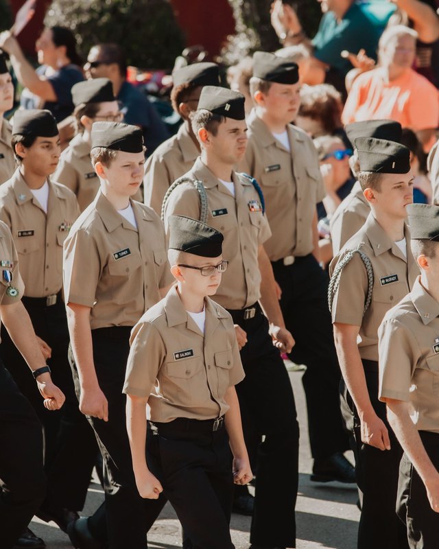 Uniformed cadets marching in the Chapin Labor Day parade past spectators.