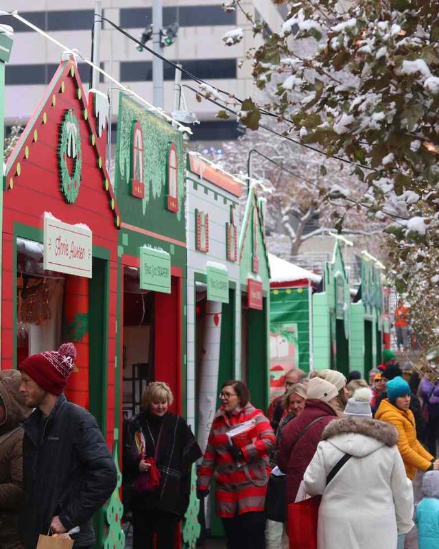 Shoppers browsing green and red holiday storefronts at a snowy Christmas village, likely the Hallmark Christmas Experience.