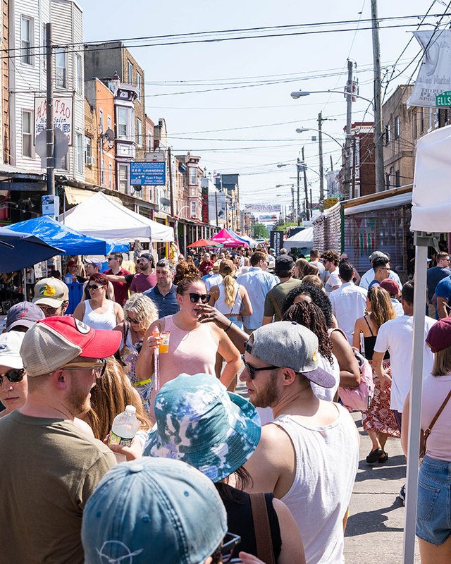 Crowd of shoppers browsing market stalls with white tents along a South 9th Street block