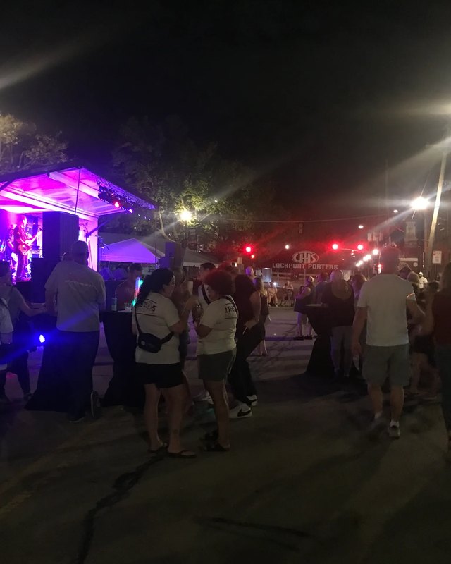Night street crowd gathered around a pink-lit stage at the Taste of Lockport festival in downtown Lockport.