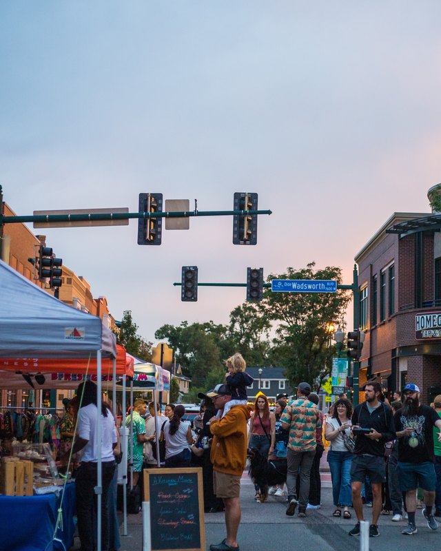 Evening street fair in Olde Town Arvada with vendor tents and crowds of shoppers along the street.
