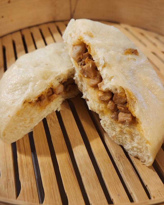 Two steamed buns cut open to show savory filling, resting on a bamboo steamer.