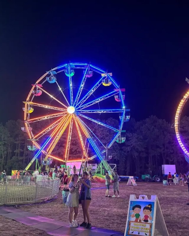 Night view of the Ocean County Fair with a lit ferris wheel, rides and visitors on the fairground.
