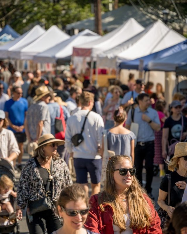 Crowds of shoppers walking past white market tents at the Takoma Park Street Festival.