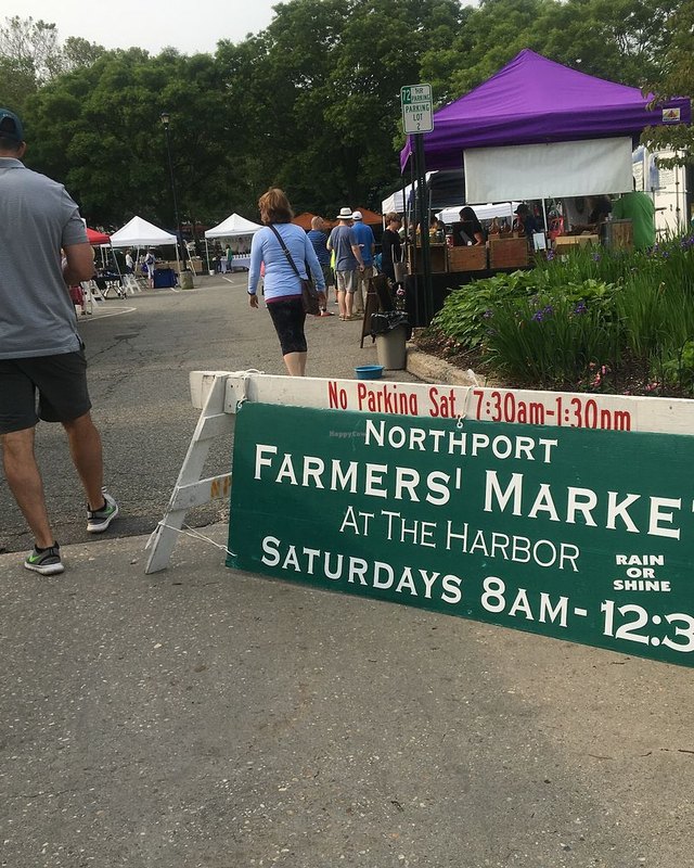 Shoppers and a purple vendor tent at the Northport Farmers' Market sign at the harbor.