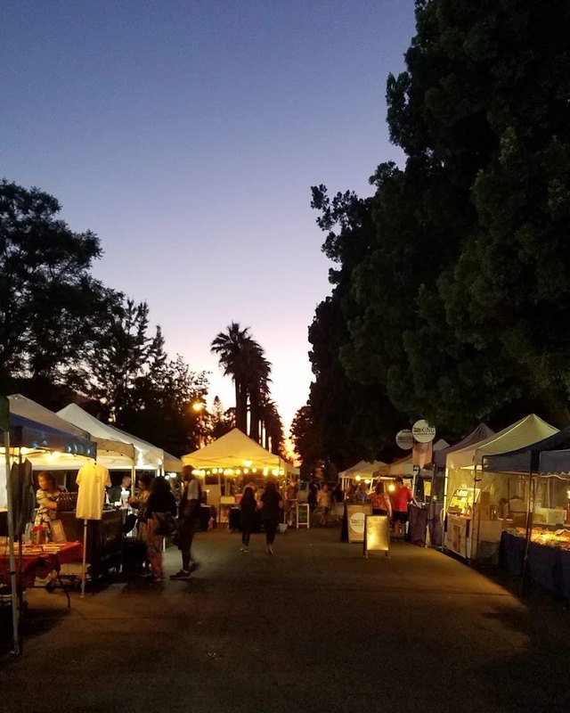 Evening view of tents and shoppers lining the San Dimas Farmers Market aisle at dusk.