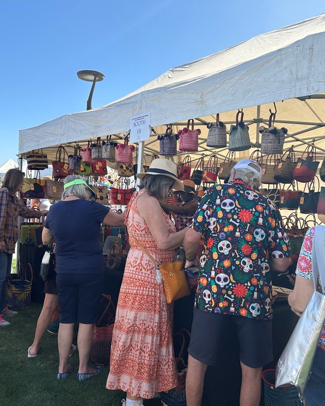 Shoppers gathered at a market booth with hanging baskets under a white tent at the festival.