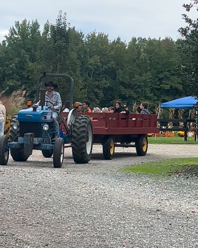 Blue tractor pulling a red hayride wagon with riders along a gravel farm lane at Chapel Hills Farm