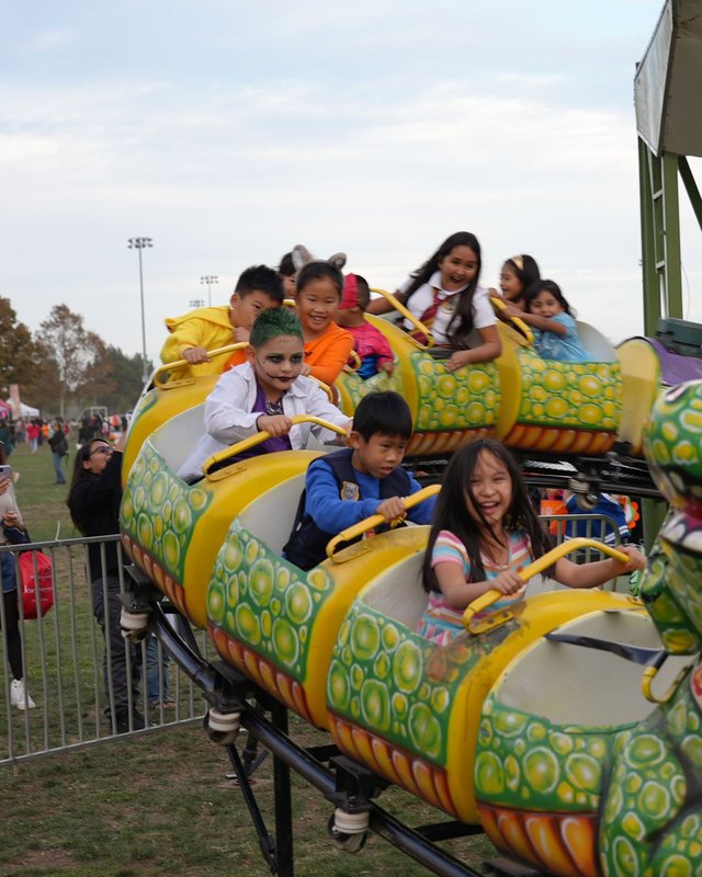 Children riding a painted dragon-shaped ride at the Halloween Spooktacular, with a crowd of visitors around.