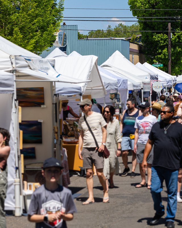 Crowds walking past white craft vendor tents at the St. Johns Bizarre street fair.