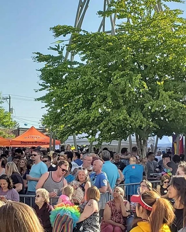 Crowd of people gathered among festival tents and shade trees at an outdoor Burien Pride event.