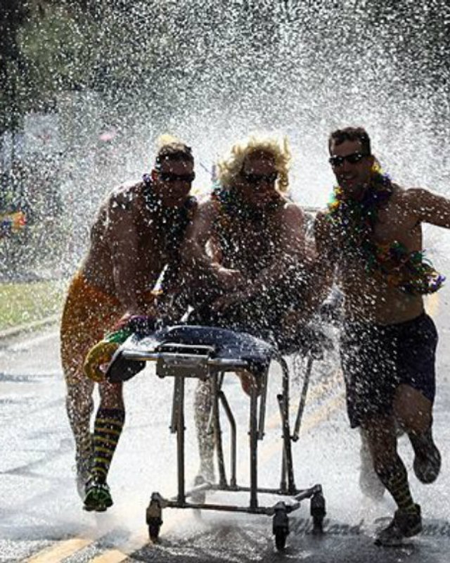 People running through a water spray pushing a grill cart on a street during a summer festival.