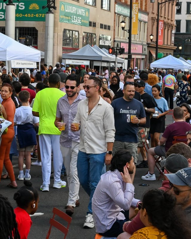Crowd of shoppers walking past white tent booths along a city street during Hartford Taste.