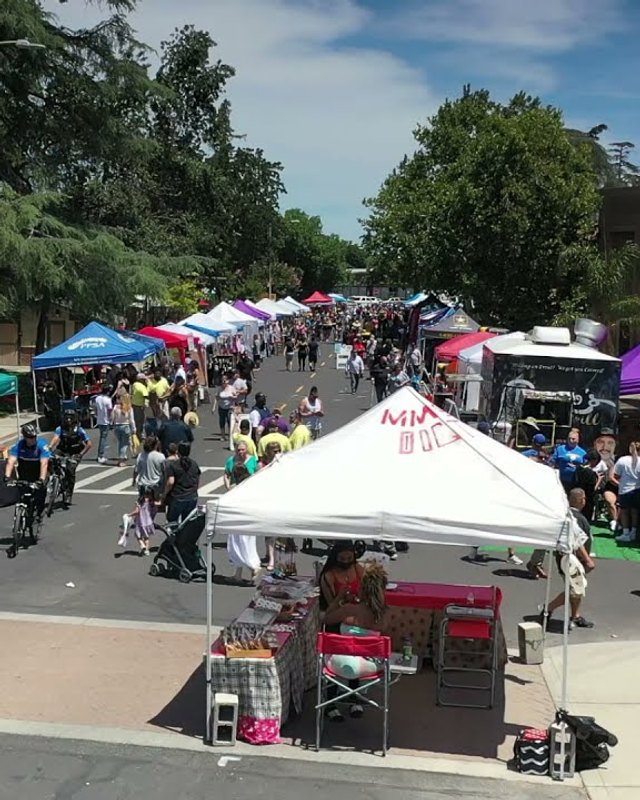 Street fair with blue, green and purple tents and shoppers along a downtown Manteca street.