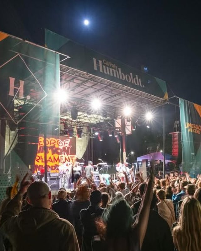 Night crowd with raised hands in front of a lit outdoor festival stage