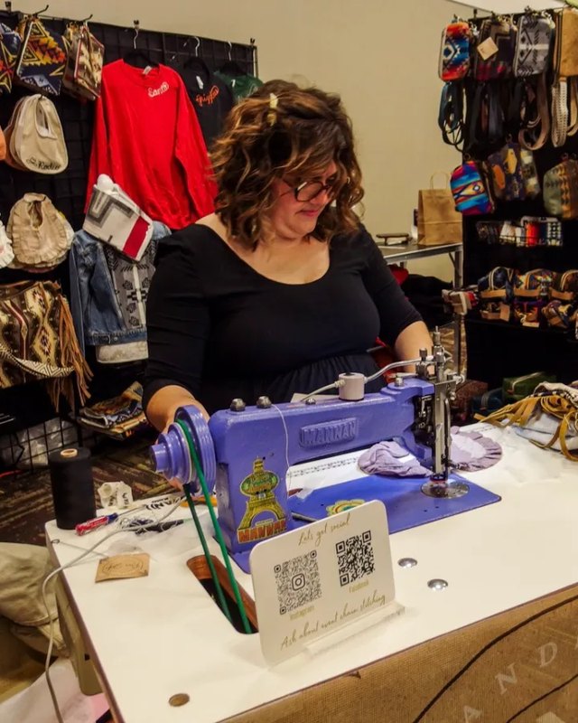 Vendor sewing leather goods at a booth stocked with bags and wallets at Wintry Market