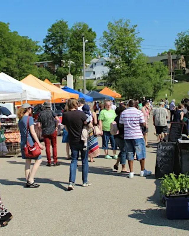 Shoppers walking among white tents and market booths on a sunny day outdoors.