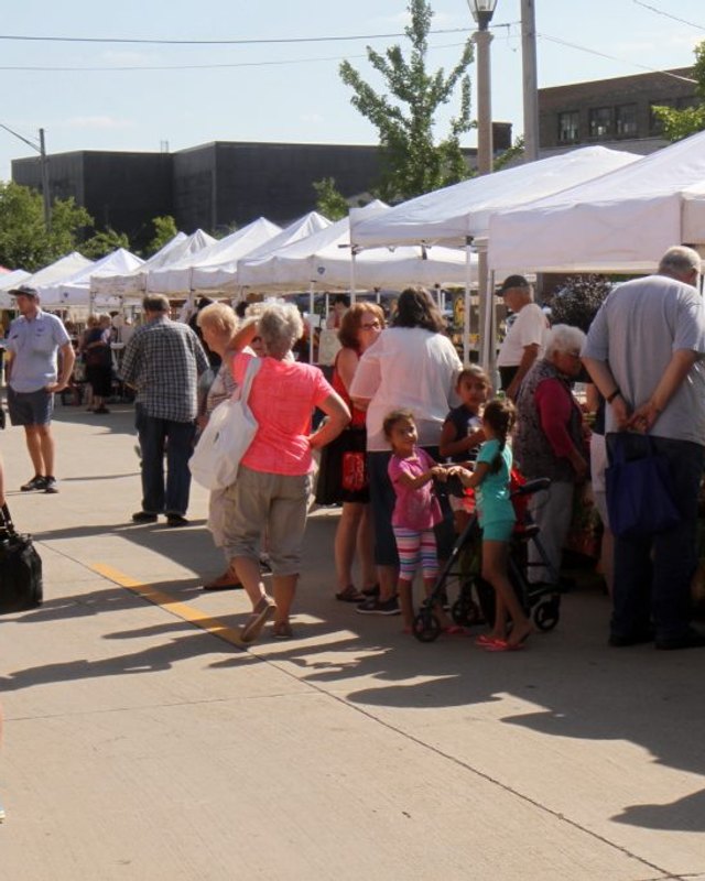 Shoppers walking past white market tents along a sidewalk at the South Milwaukee Downtown Market.