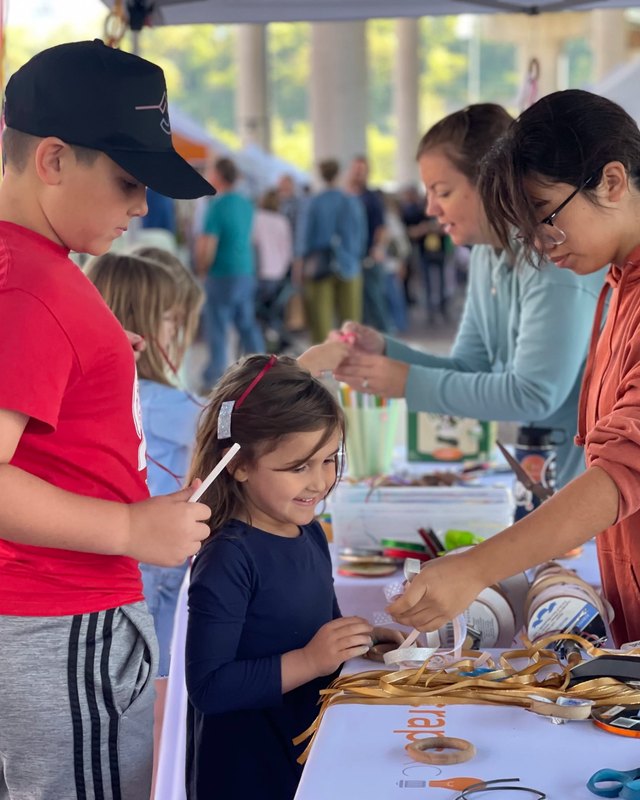 Children and adults working with ribbons and craft supplies at an outdoor craft booth
