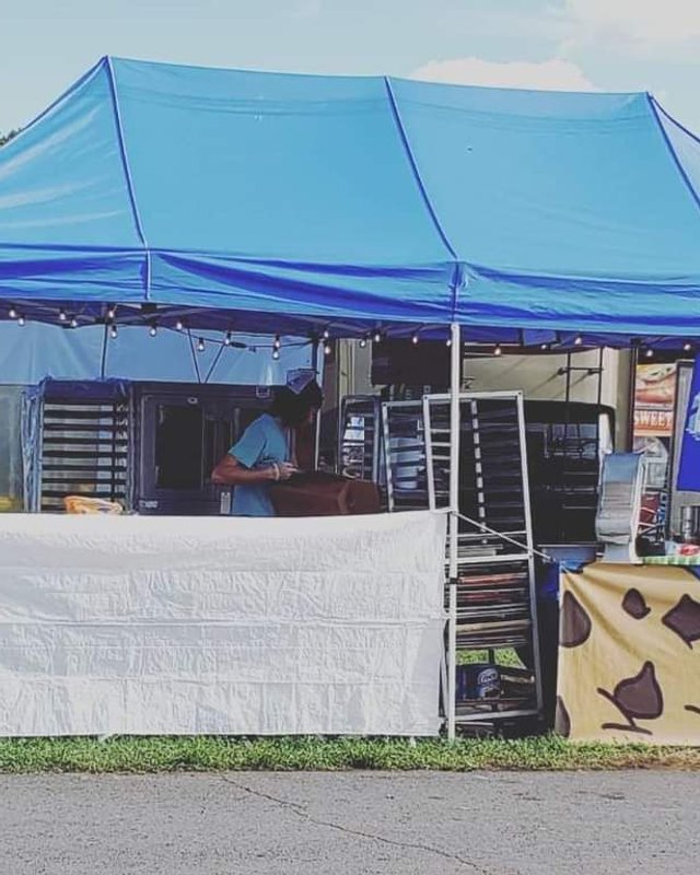 Vendor food booth under a blue tent at the Montgomery County Agricultural Fair, with a worker behind the counter.