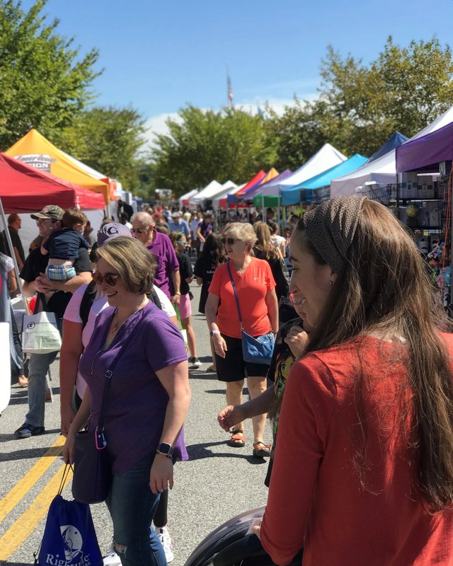 Crowd of shoppers walking past white and colorful vendor tents at an outdoor street festival.