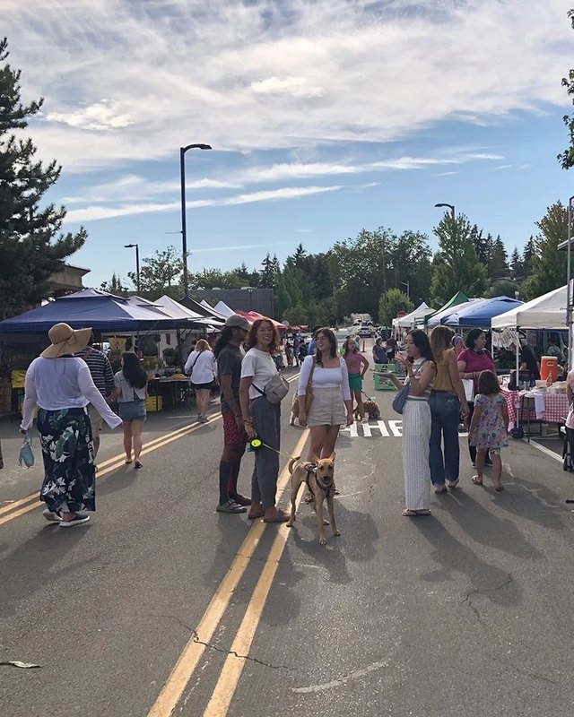 Shoppers and vendor tents lining a sunny street at the Kenmore Farmers Market