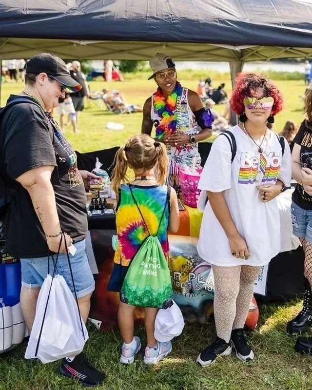 Festival visitors gathered around a booth tent on a grassy park field at the Jersey Gay Pride event.
