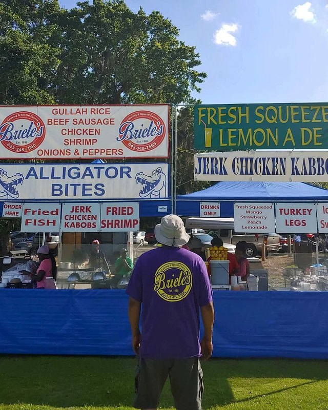 Food booths with menu signs and a vendor in a purple shirt at the Gullah festival