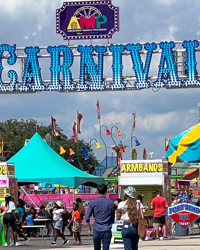 Crowds walking past colorful booths and the Carnival sign at the Fort Bend County Fair