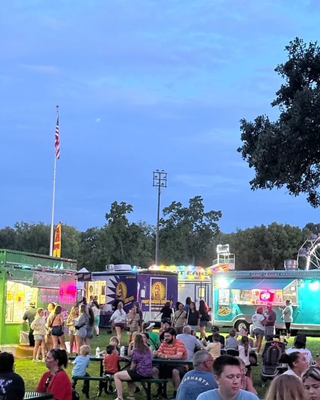 Evening crowd at food trucks and carnival-style vendor stands with string lights, at the Wilmington Catfish Days festival.