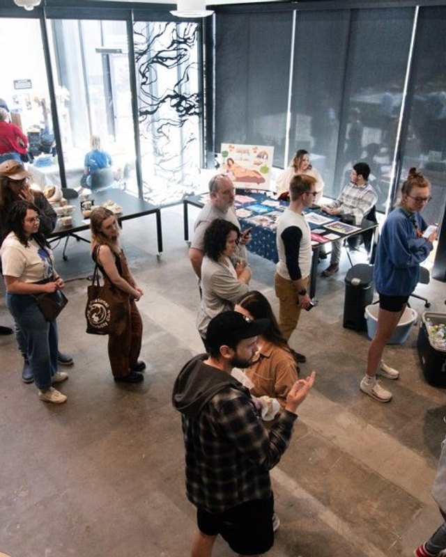 Shoppers browsing tables at an indoor artist market inside a bright gallery space.
