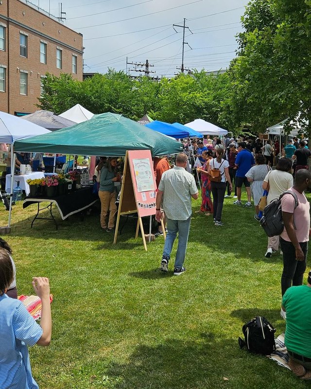Shoppers browsing tents and market stalls on a grassy lawn at the SoNo Saturday Market