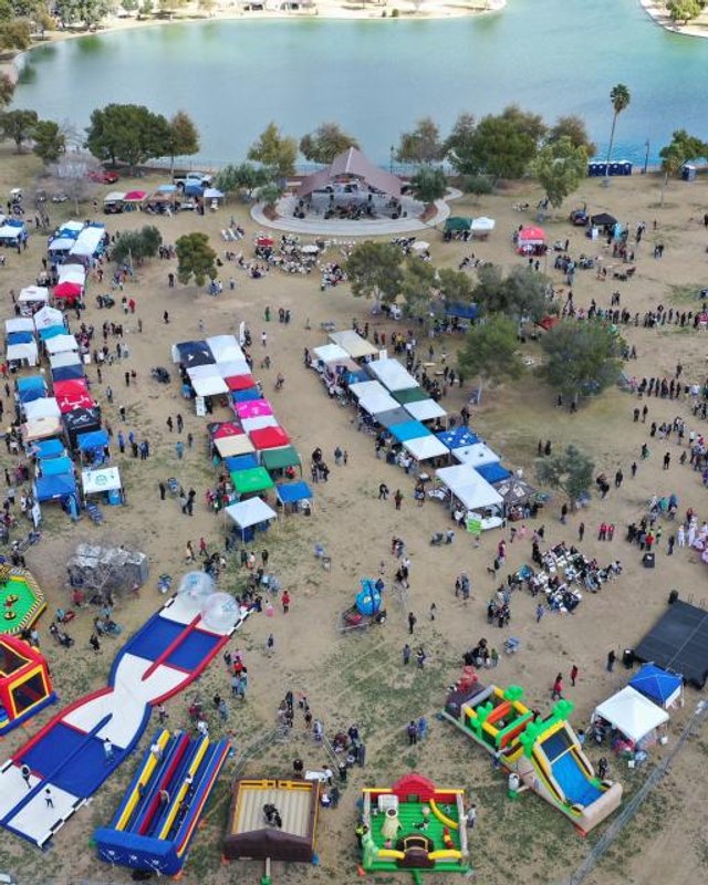 Aerial view of the Laveen BBQ festival with rows of vendor tents, inflatable games and crowds at the lakeside park