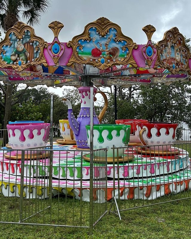 Colorful antique-style carousel teacup ride with a decorative canopy on grass at a park.