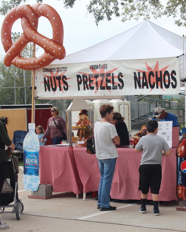 Food booth with a giant pretzel sign and nuts, pretzels and nachos menu, with shoppers at a Eureka Days vendor tent.