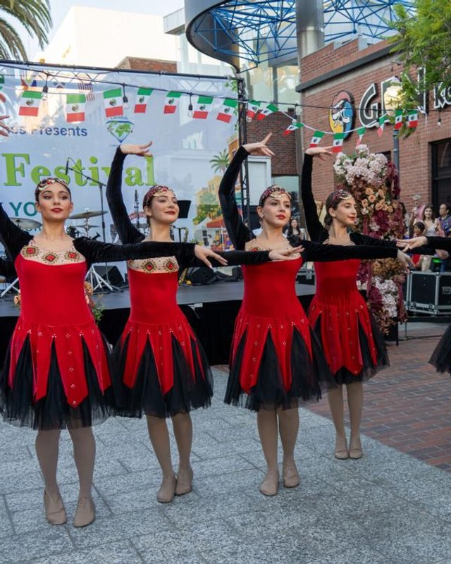 Costumed dancers in red and black performing on a street during a festival with banners overhead.