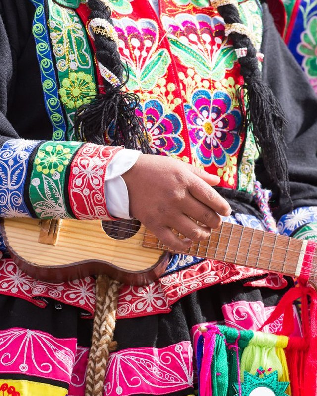 Colorful embroidered traditional dress and a small guitar-like instrument, a detail of Latin American folk culture.