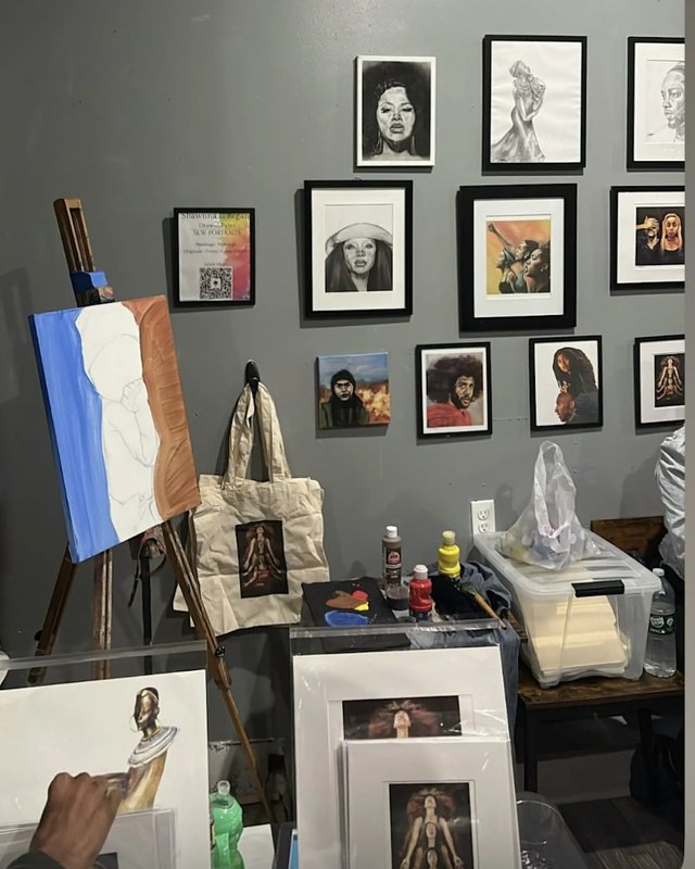 Framed portrait artwork and tote bags displayed on a gallery wall and table at the event space