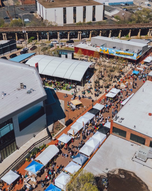 Aerial view of the Paristown market with rows of vendor tents and crowds on the brick plaza.