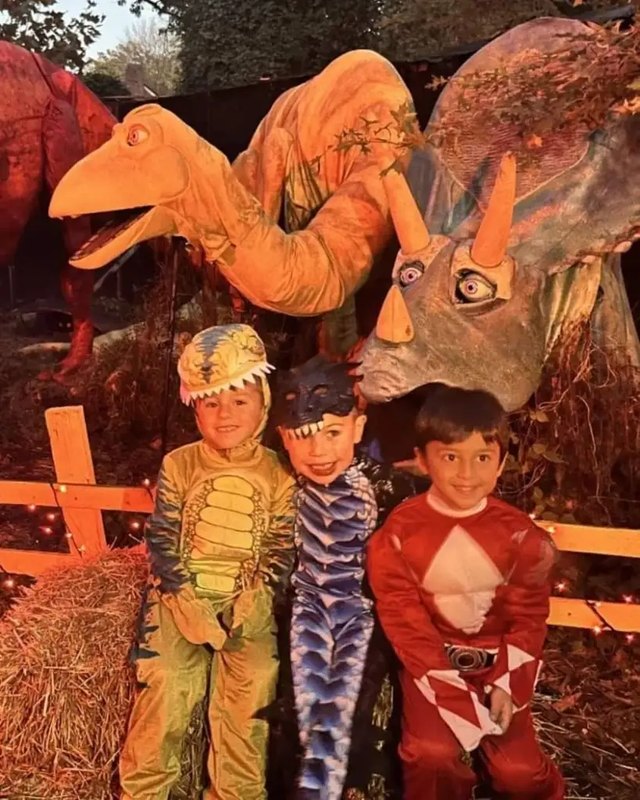 Children in costumes posing in front of large dinosaur figures at the Spooky Fest display.