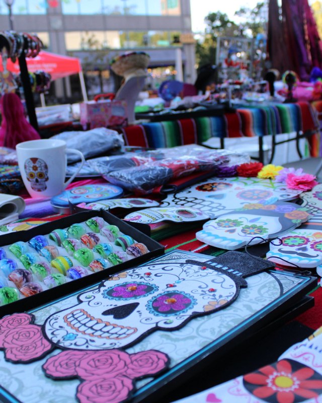 Vendor tables with colorful sugar skull merchandise and serape cloths at a street market