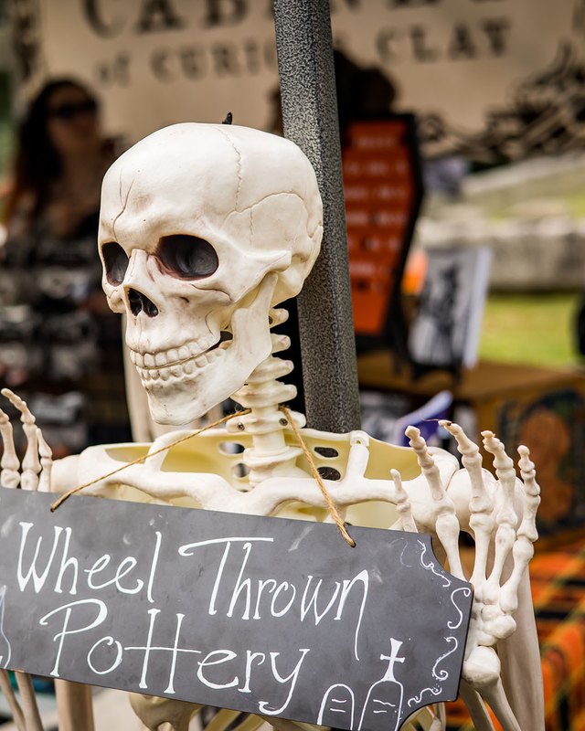 Skeleton prop beside a Wheel Thrown Pottery sign at a market booth with orange decorations.